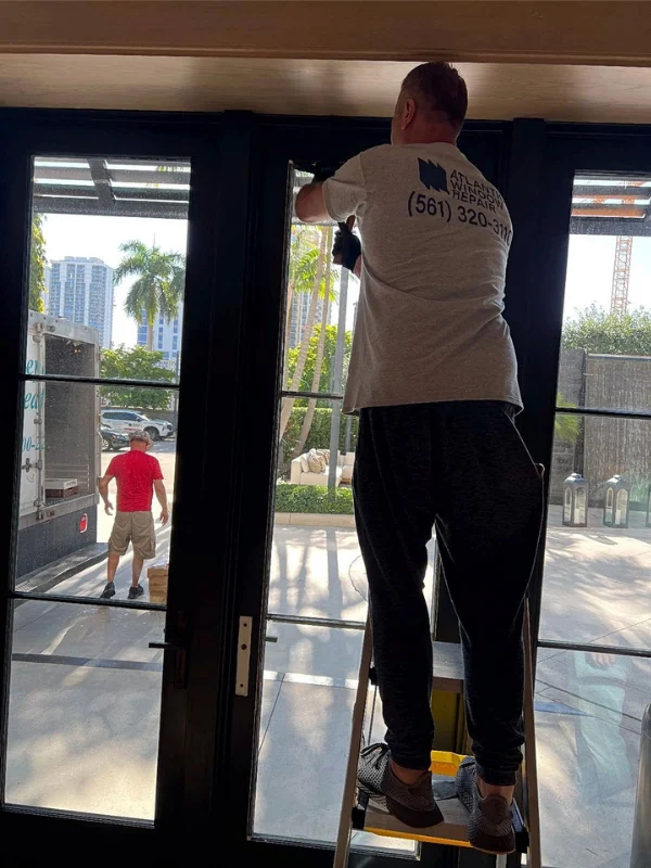 Technician on a ladder working on a tall glass door