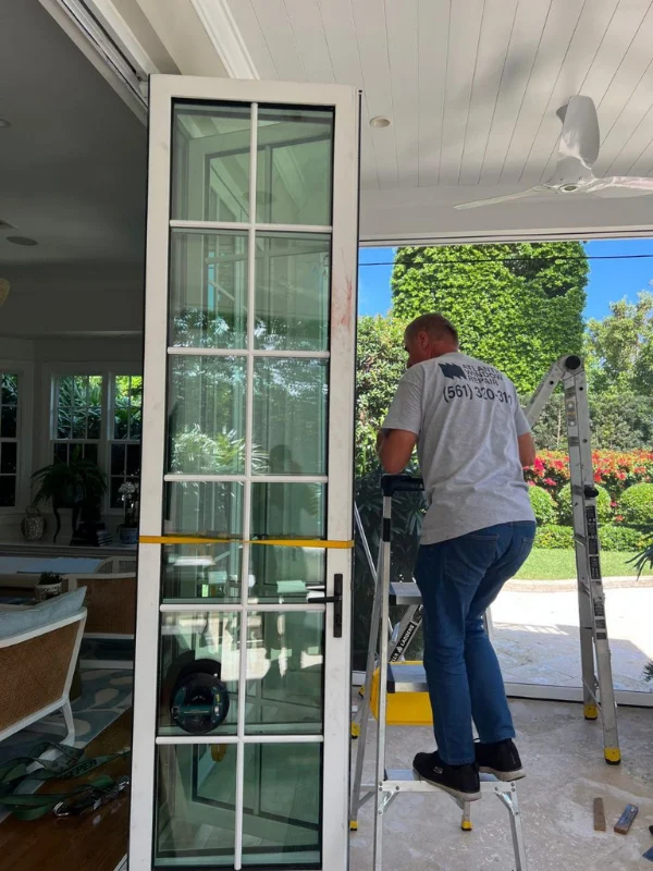 Technician on a ladder installing a tall glass door unit