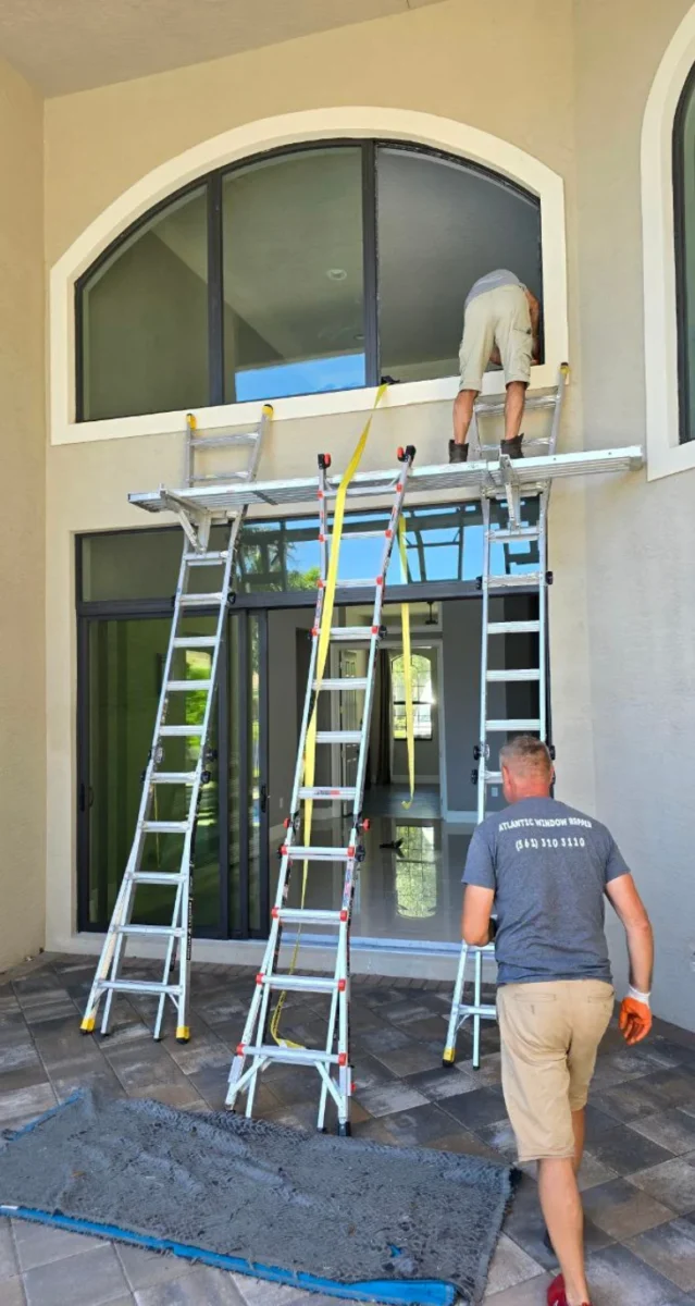 Technician with extension ladders at a two-story glass facade