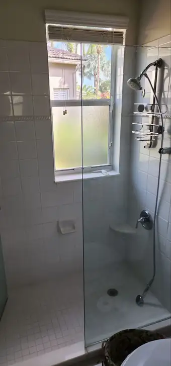 Frameless glass shower panel next to a frosted window in a bathroom, shower door installation in Boca Raton